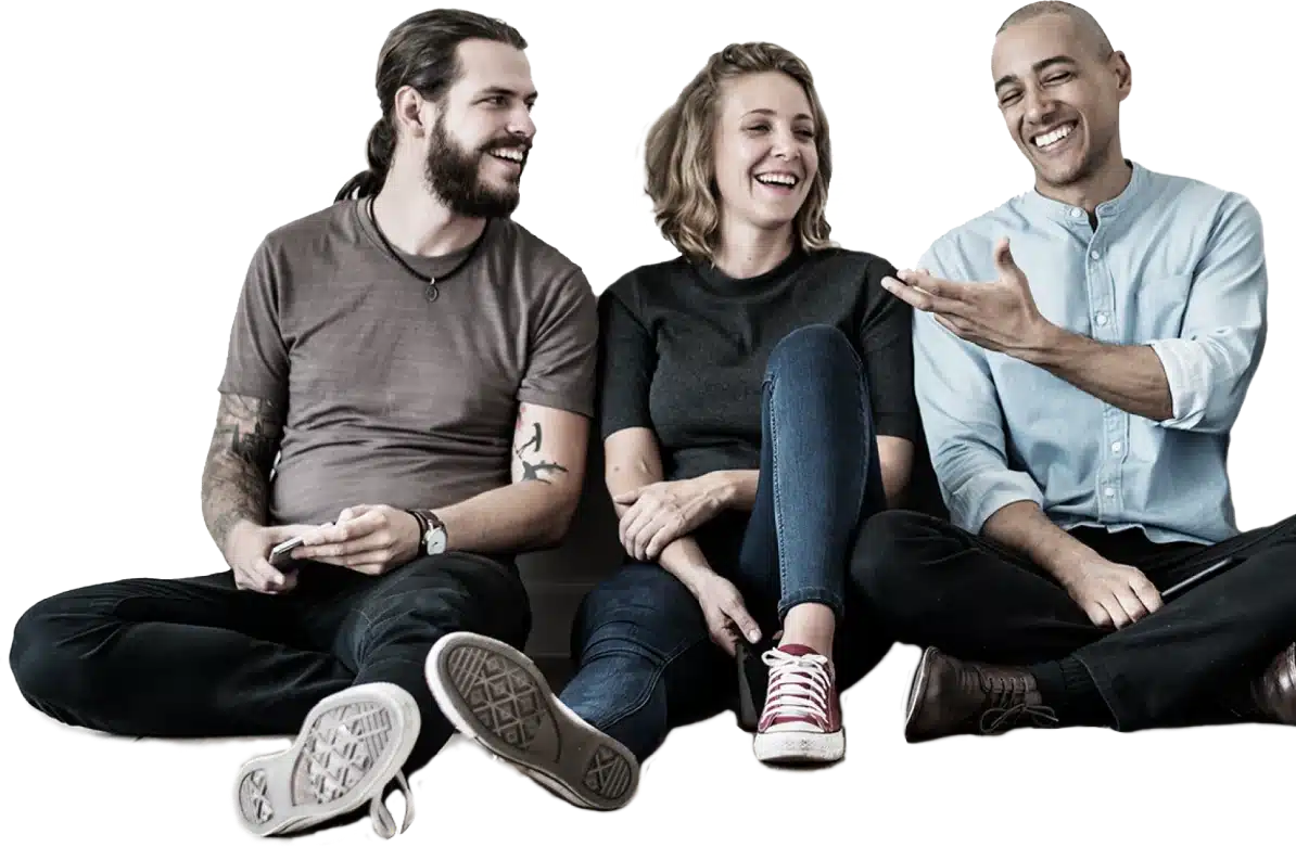 Three People Sitting On The Floor Laughing And Talking. The Person On The Left Has A Beard And Long Hair, The Person In The Middle Has Shoulder-Length Hair, And The Person On The Right Has A Shaved Head. They Appear To Be Enjoying A Relaxed And Friendly Conversation—Meet The Dragonfly Team. Three people sitting on the floor laughing and talking. The person on the left has a beard and long hair, the person in the middle has shoulder-length hair, and the person on the right has a shaved head. They appear to be enjoying a relaxed and friendly conversation—meet the Dragonfly Team.