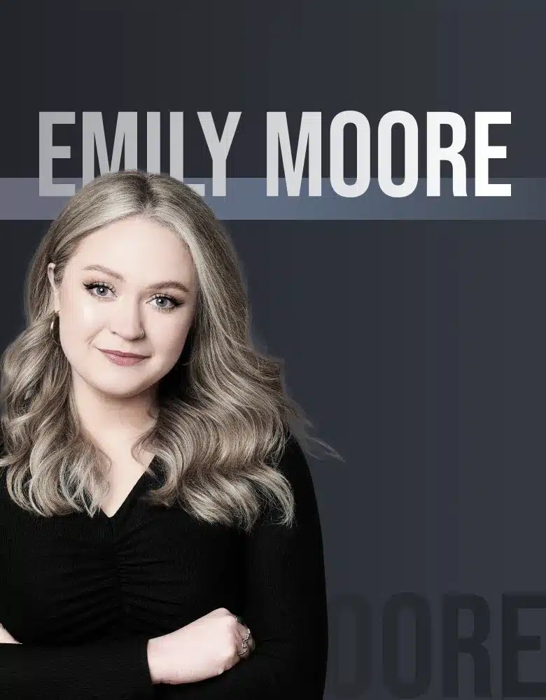 A Woman With Long Wavy Blonde Hair, Wearing A Black Top, Is Posed In Front Of A Dark Gradient Background. The Text &Quot;Emily Moore - Dragonfly Team&Quot; Is Displayed Prominently Above Her. She Smiles Subtly With Her Arms Folded. A woman with long wavy blonde hair, wearing a black top, is posed in front of a dark gradient background. The text "EMILY MOORE - Dragonfly Team" is displayed prominently above her. She smiles subtly with her arms folded.