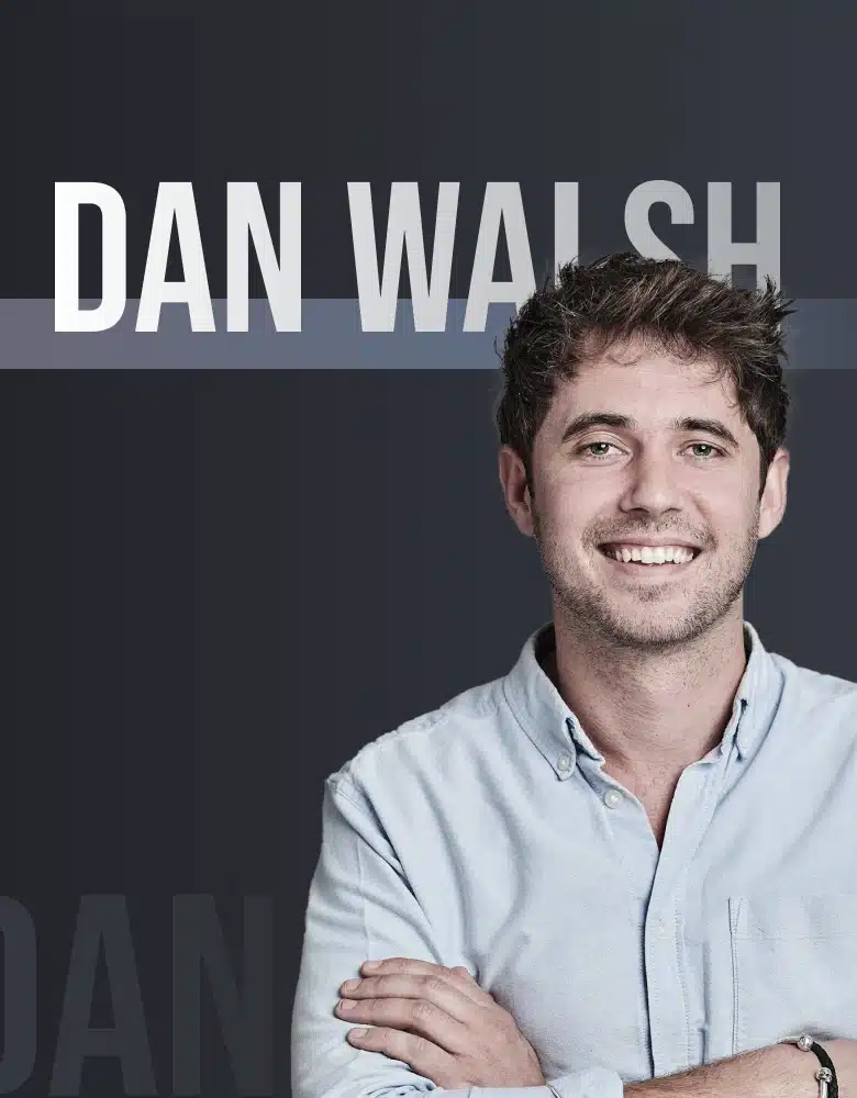 A Man With Short Dark Hair And A Beard Is Smiling While Looking Directly At The Camera. He Is Wearing A Light Blue Button-Up Shirt And Has His Arms Crossed. The Background Is Dark Gray With The Name &Quot;Dan Walsh&Quot; In Large White Text At The Top, Introducing Him As Part Of The Dragonfly Team. A man with short dark hair and a beard is smiling while looking directly at the camera. He is wearing a light blue button-up shirt and has his arms crossed. The background is dark gray with the name "DAN WALSH" in large white text at the top, introducing him as part of the Dragonfly Team.