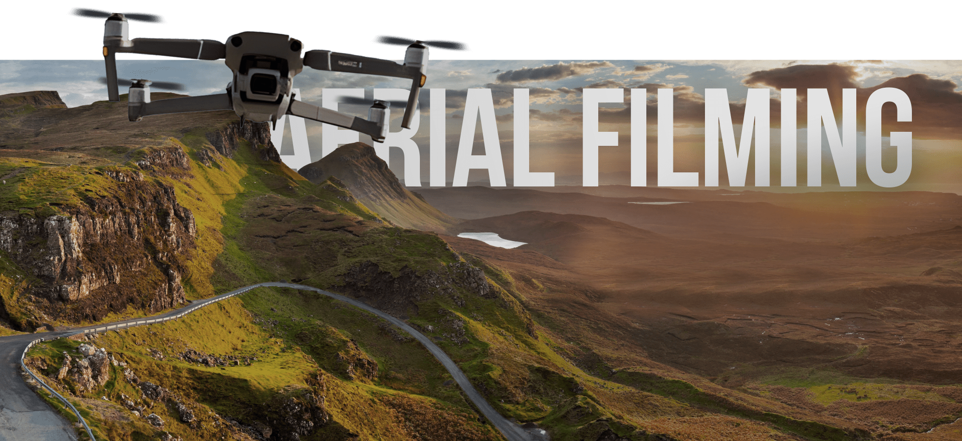 A Drone Is Flying Over A Scenic Landscape Of Rolling Green Hills And Rugged Cliffs, With A Winding Road Visible Below. The Text &Quot;Aerial Filming&Quot; Is Prominently Displayed In The Background Against A Sky At Sunset. A drone is flying over a scenic landscape of rolling green hills and rugged cliffs, with a winding road visible below. The text "AERIAL FILMING" is prominently displayed in the background against a sky at sunset.