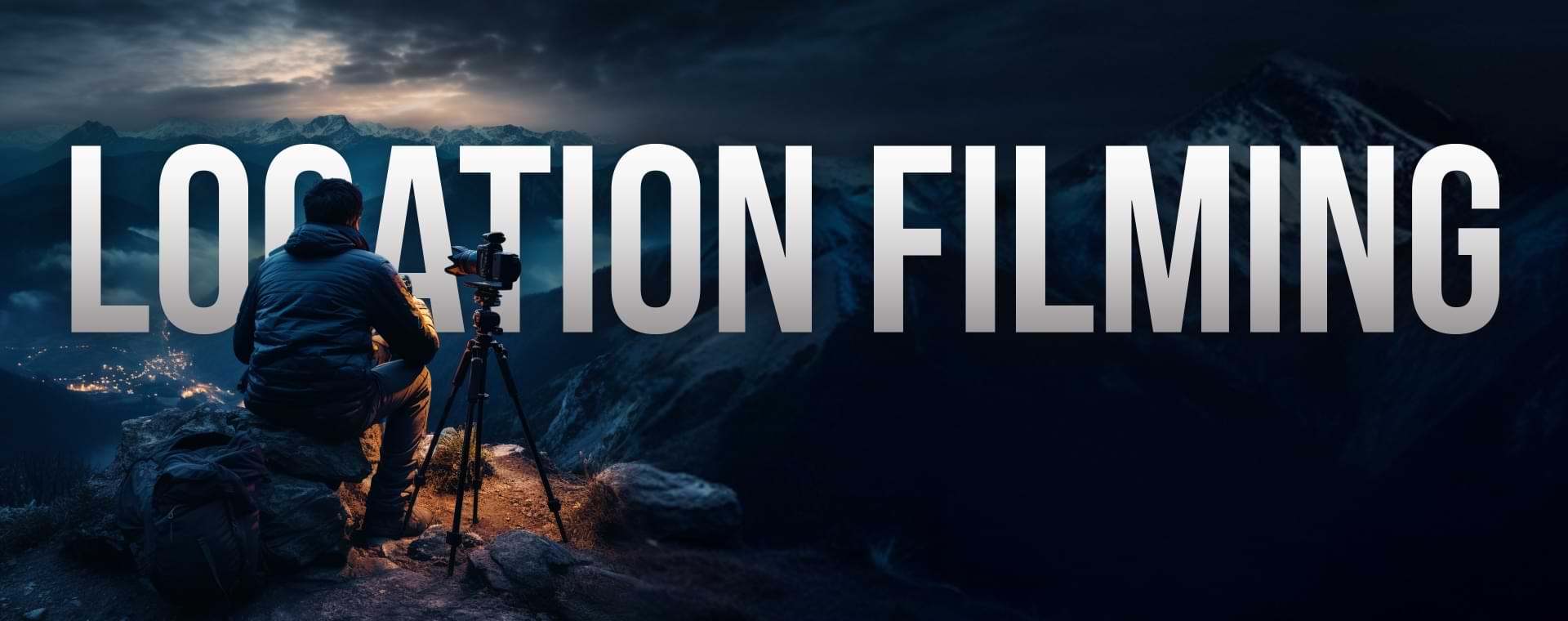 A Person With A Camera On A Tripod Sits On A Mountainside At Dusk, Capturing A View Of A Village Below And Mountains In The Distance. &Quot;Location Filming&Quot; Is Prominently Written In Large, Bold Letters Across The Image. A person with a camera on a tripod sits on a mountainside at dusk, capturing a view of a village below and mountains in the distance. "LOCATION FILMING" is prominently written in large, bold letters across the image.