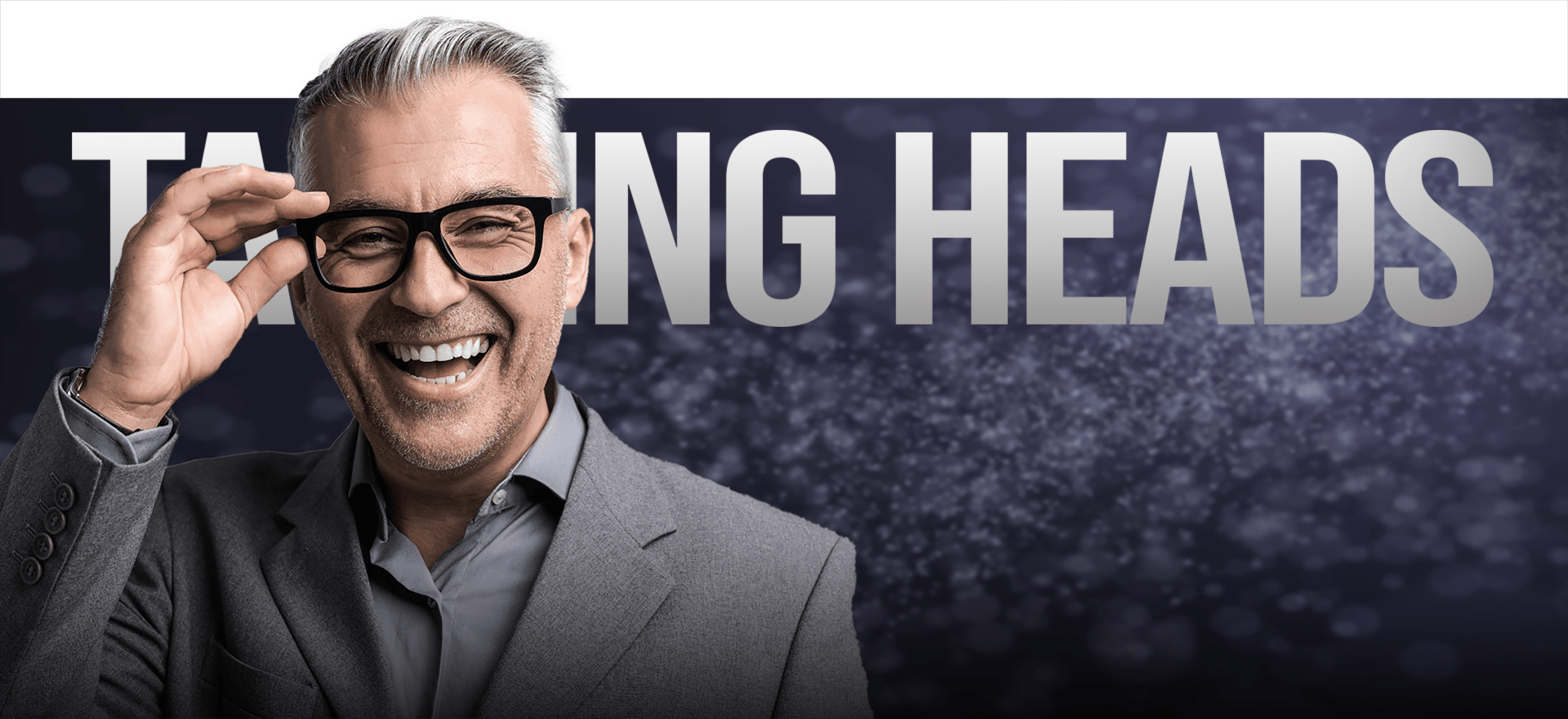 A Middle-Aged Man With Gray Hair And Glasses Is Smiling Broadly. He Is Wearing A Gray Suit. Behind Him, There Is A Background With Sparkling Dark Blue And Purple Tones, And Partially Visible Large Text That Reads &Quot;Talking Heads. A middle-aged man with gray hair and glasses is smiling broadly. He is wearing a gray suit. Behind him, there is a background with sparkling dark blue and purple tones, and partially visible large text that reads "TALKING HEADS.